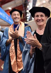 Two robed faculty members smile and clap